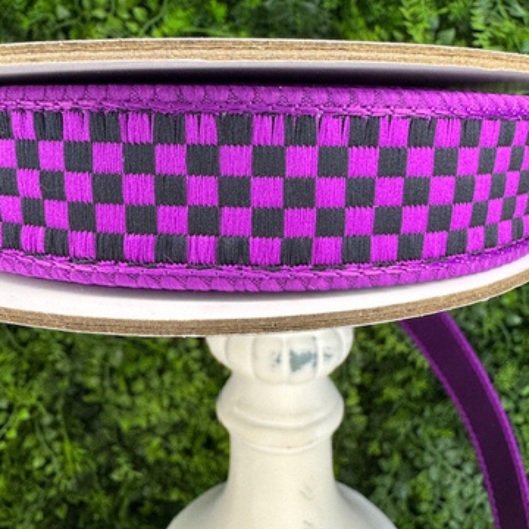 Purple and black checkered Farrisilk ribbon on a spool with a white stand against a green grass background