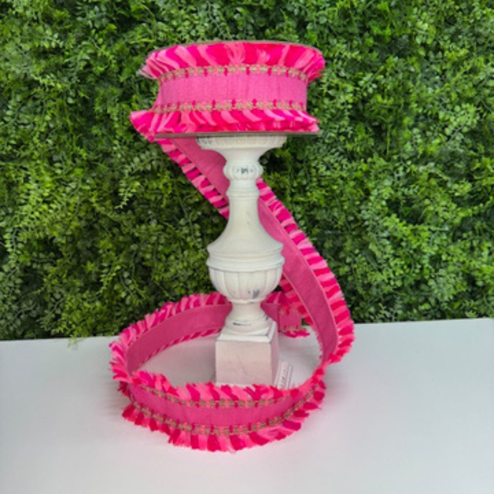 Decorative pink Farrisilk ribbon with ruffled details on a white surface against a green leafy background