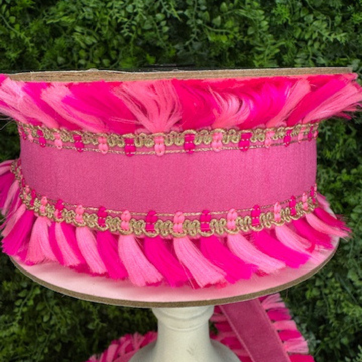 Pink decorative Farrisilk riibbon with tassels and a gold band on a stand against a green background