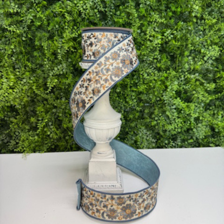 Decorative Farrisilk ribbon with blue floral pattern on a white pedestal against a green foliage background