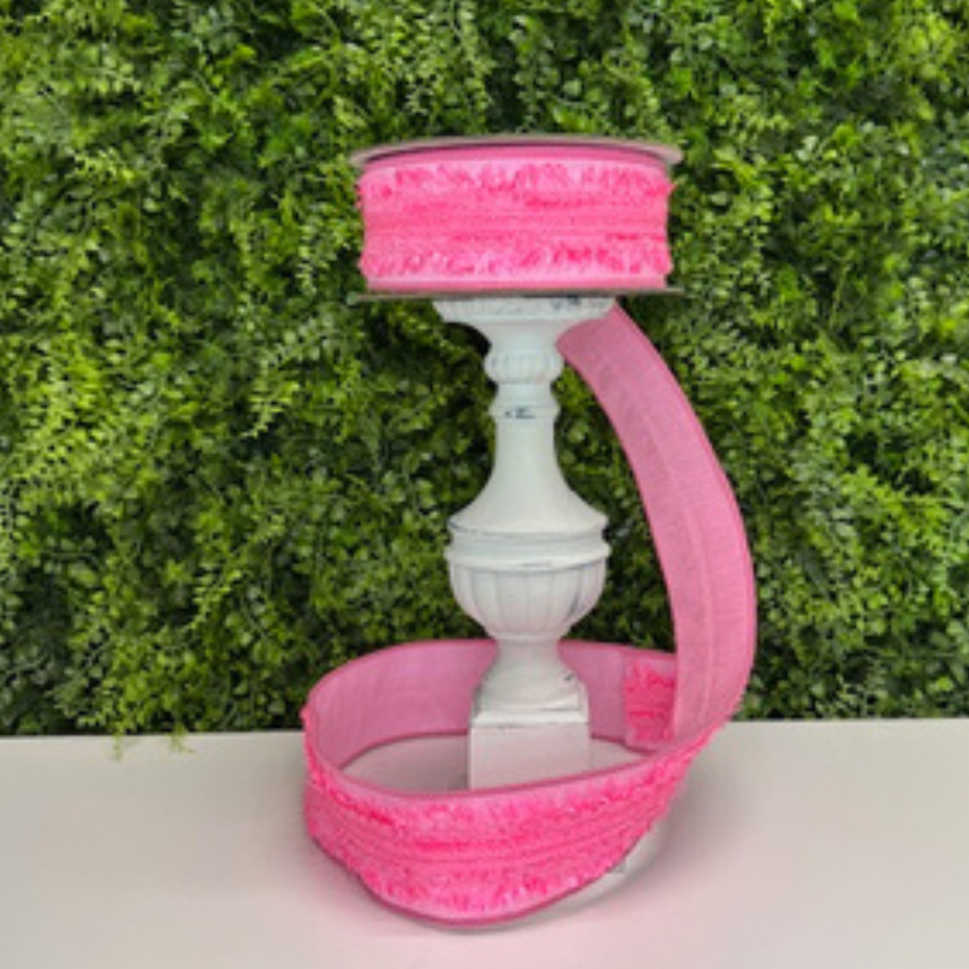 Pink ribbon on a white candle holder against a green leafy background