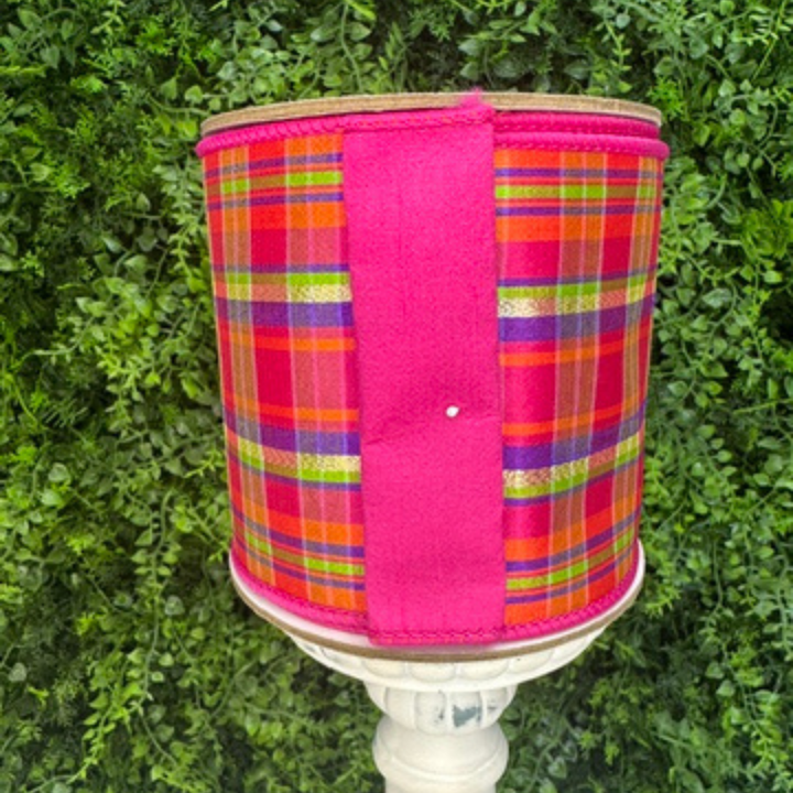 Colorful plaid ribbon with a pink border on a white pedestal against a green leafy background