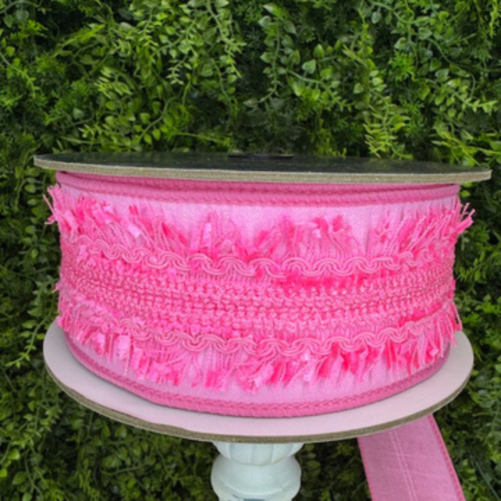 Spool of pink lace ribbon on a white stand with a green leafy background