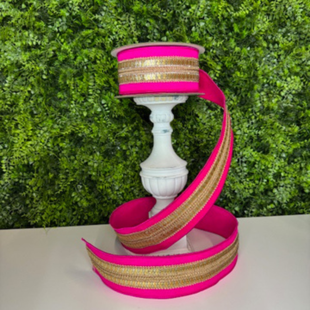 Pink and gold ribbon on a white candle holder against a green bush background