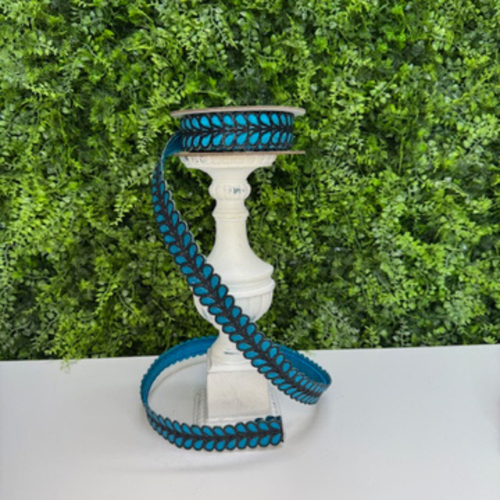 Blue and black decorative Farrisilk ribbon on a white pedestal against a green hedge background