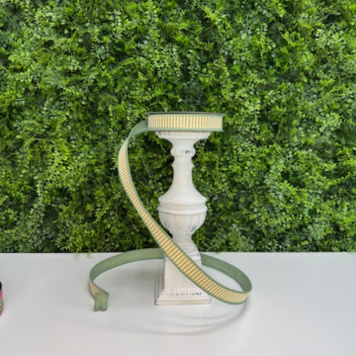 Farrisilk Yellow and white striped ribbon with green back and edging on a white surface against a green leafy background