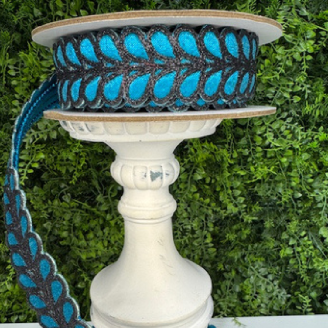 Spool of Farrisilk blue and black ribbon on a decorative stand with green foliage in the background