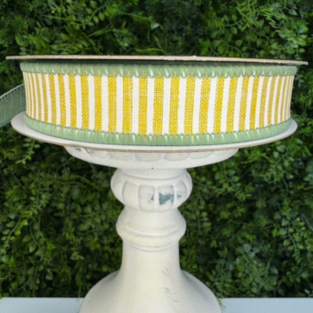 Striped Farrisilk yellow and White striped ribbon with green back on a decorative stand with a green foliage background