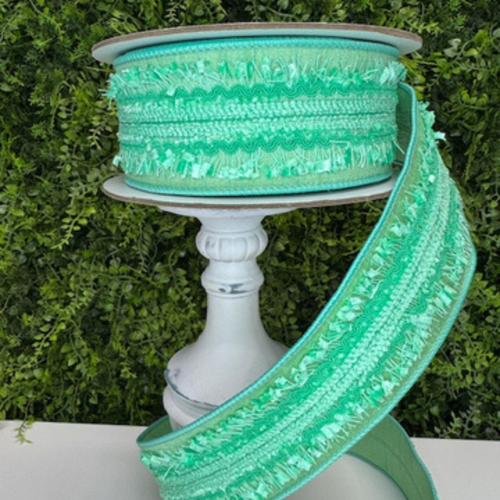 Spool of mint green decorative ribbon on a white pedestal with a green leafy background