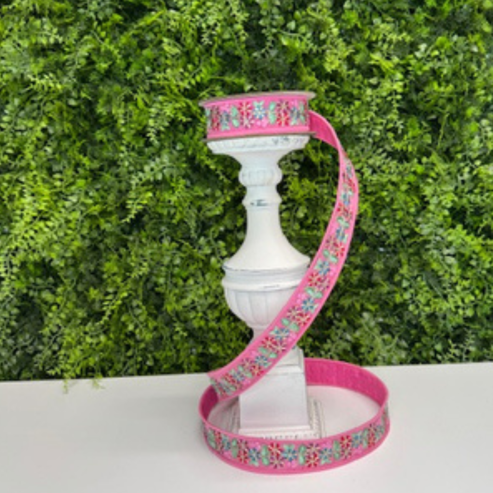 Pink floral ribbon tied around a white decorative object with a green leafy background