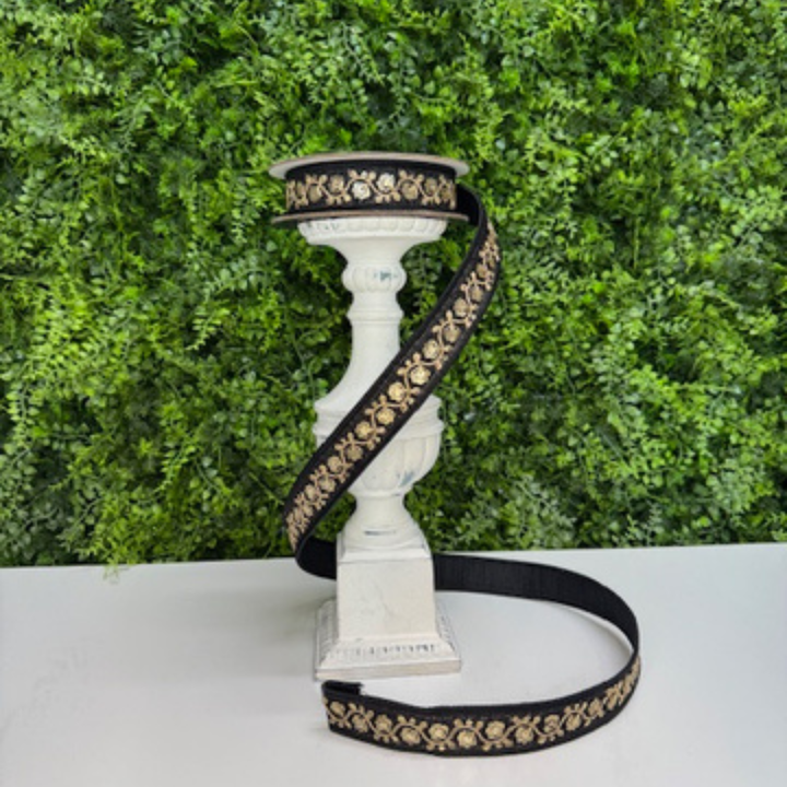 Farrisilk black ribbon with gold floral patterns on a white pedestal against a green foliage background