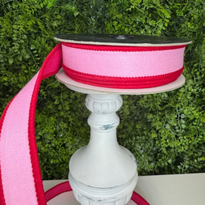 Spool of pink ribbon on a white stand with a green foliage background