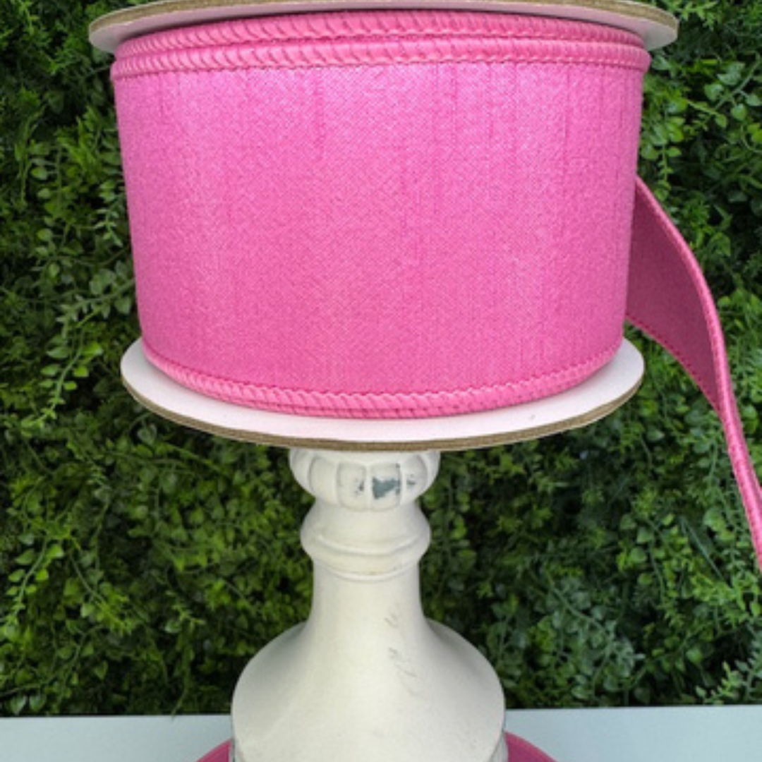 Spool of Farrisilk pink ribbon on a white stand with a green leafy background