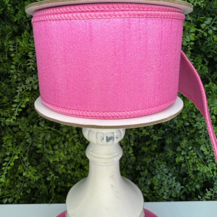 Spool of Farrisilk pink ribbon on a white stand with a green leafy background