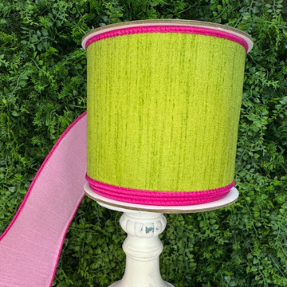 Spool of Farrisilk green ribbon with pink edge on a white stand against a green leafy background