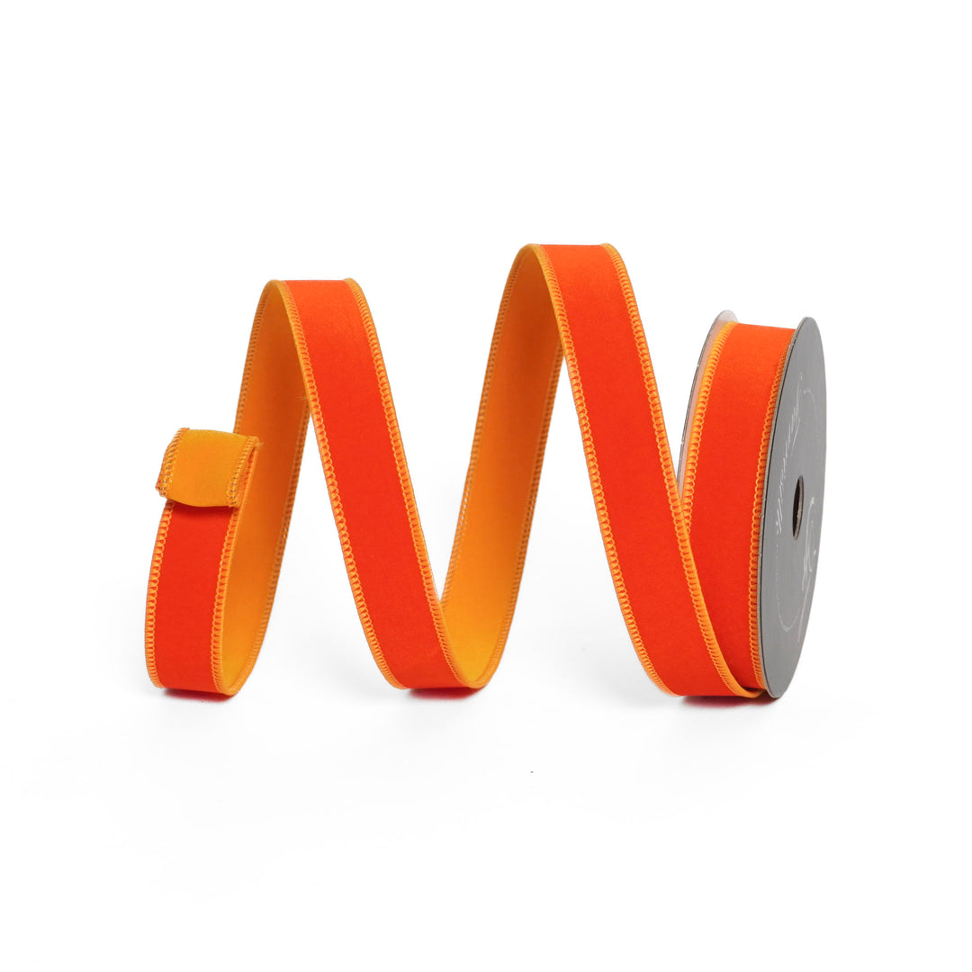 Orange ribbon with a yellow back on a spool against a white background